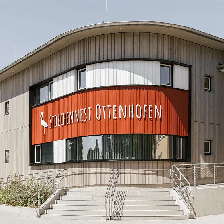 Außenansicht der Kinderkrippe Storchennest Ottenhofen mit Eingangsbereich, Treppe und Gebäudeschriftzug.